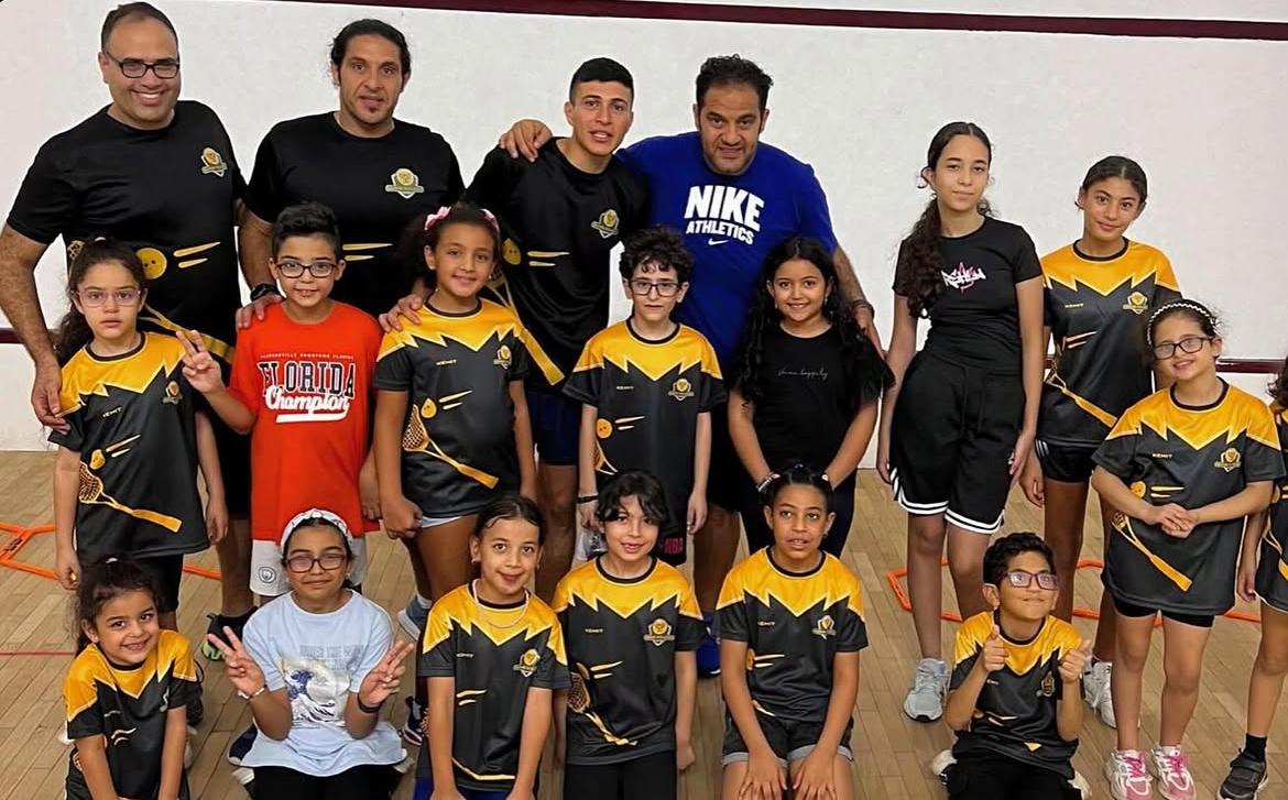 Coach Ezz with a group of students on a squash court